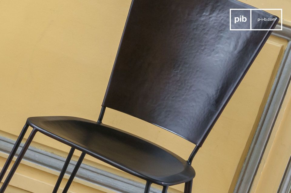 La silla de metal tiene hermosos reflejos en tono berenjena que muestran la superficie golpeada a mano.